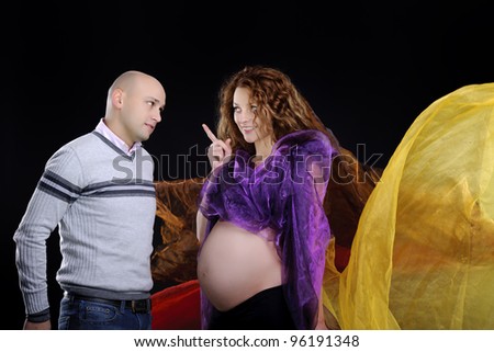 happy young family expecting a baby and posing on black background