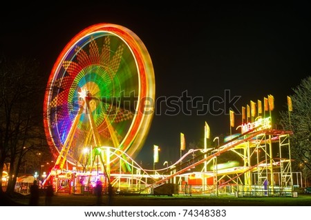 Amusement park at night - ferris wheel and rollercoaster in motion