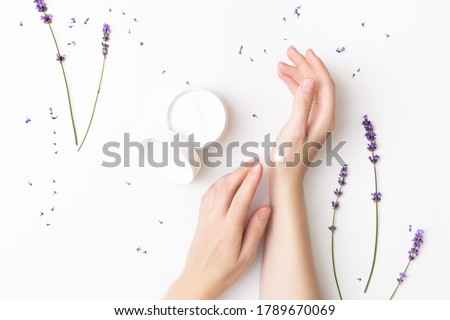 Beautiful well-conditioned female hands moisturizing cream surrounded with lavender flowers on the white background. Hand and body care concept Сток-фото © 