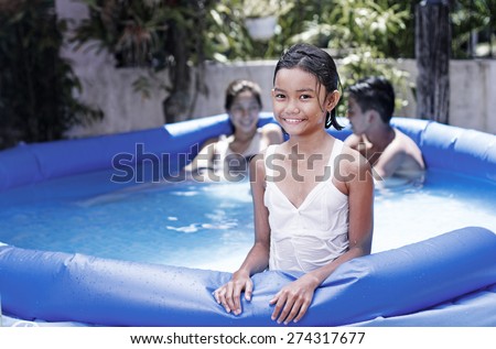 Happy young asian girl enjoying an outdoor summer bath on an inflatable swimming pool.
