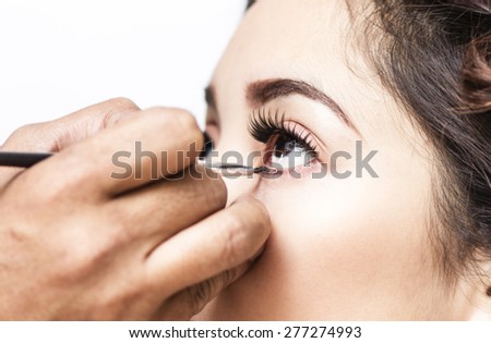 Makeup artist applying mascara on a lady inside a beauty parlor. Close up.