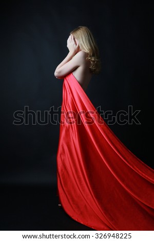 Beautiful blonde woman in long flowing red silk dress. Dark background.