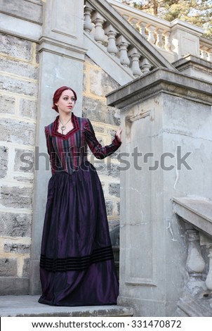 Full Length Portrait of a beautiful red haired girl wearing  Gothic inspired Victorian era clothes. walking down a stone castle staircase.