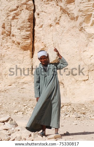 VALLEY OF THE KING - NOVEMBER 20: Young archaeological Egyptian worker with rock on his shoulder on November 20, 2009 in Valley of the king, Egypt