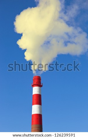 Red and white factory chimney with smoke against blue sky