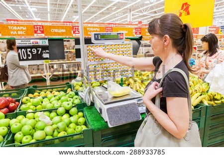 SAMARA, RUSSIA - JUNE 13, 2015: Young woman weighing bananas on electronic scales in produce department of the Auchan store
