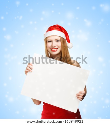 Beautiful young woman in christmas suit holding advertisement on blue snowfall background