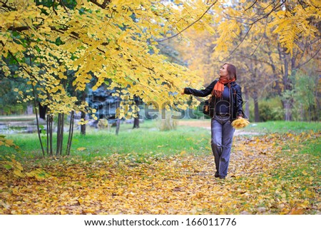 Young beautiful woman in orange scarf walking in autumnal park with a lot of fallen leaves