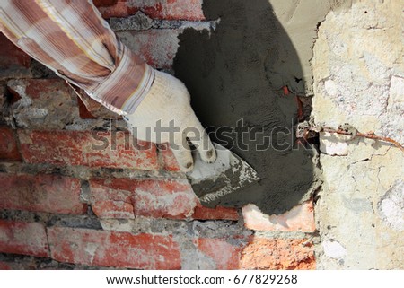 A professional builder bricklayer with hand trowel applies cement mortar to the brick wall in front of the lining during the restoration of the site in front of the cinema 商業照片 © 