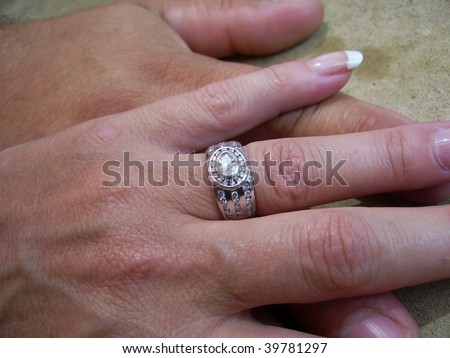 Two hands on a cement like background on top of each other showing woman\'s beautiful wedding ring