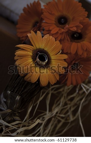 A beautiful ladies wedding ring pinned on the center of a striking orange flower among red flowers in a bouquet