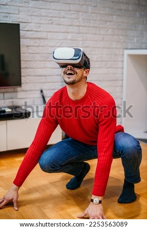 Young good looking male in a red shirt and jeans using VR glasses to explore a virtual world in his apartment. Man using virtual reality. Education and fun Imagine de stoc © 