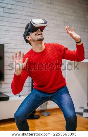 Young male in a red shirt and jeans using VR glasses to explore a virtual world in his apartment. Man using virtual reality. Education and fun Imagine de stoc © 
