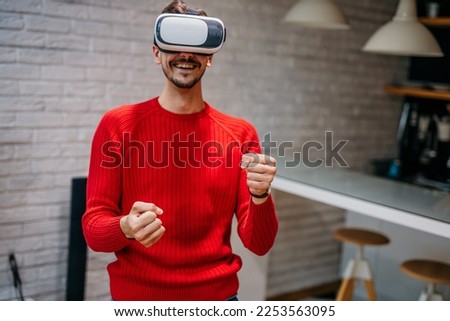 Caucasian man wearing headset glasses of virtual reality gesticulating driving with hand while standing in the living room at the house. Re-imagining Reality, VR technology of future concept. Imagine de stoc © 