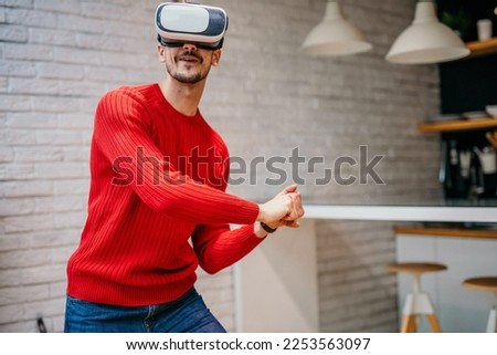 Caucasian man wearing headset glasses of virtual reality gesticulating swing with hand while standing in the living room at the house. Re-imagining Reality, VR technology of future concept. Imagine de stoc © 
