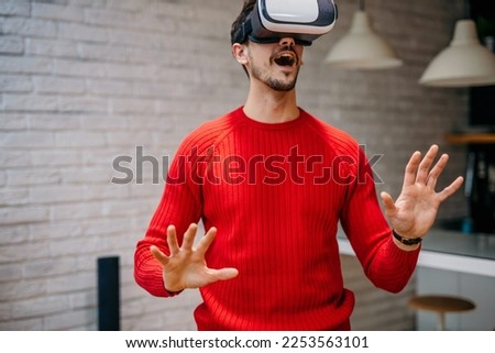 Caucasian man wearing a VR headset resting at home in the living room alone using futuristic technology making gestures with hands in the air, and playing 3D video games. Virtual reality glasses Imagine de stoc © 