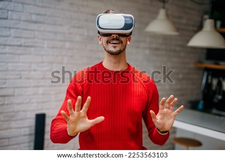Handsome man wearing a VR headset resting at home in the living room alone using futuristic technology making gestures with hands in the air, and playing 3D video games. Virtual reality glasses Imagine de stoc © 
