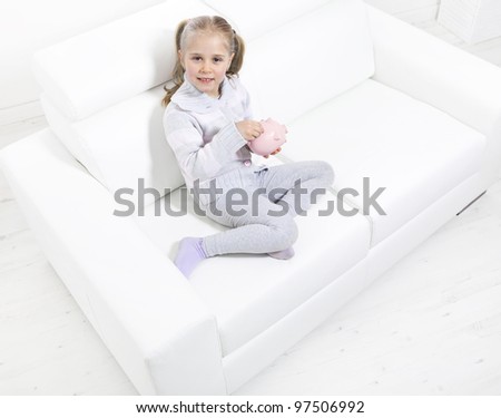 Cute little girl saving money in a piggy-bank sitting on sofa