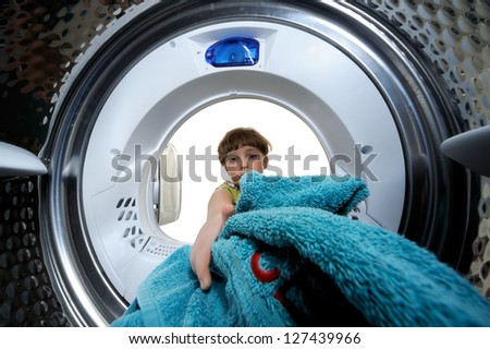 Funny boy loading clothes to washing machine. View from the inside of washing machine.