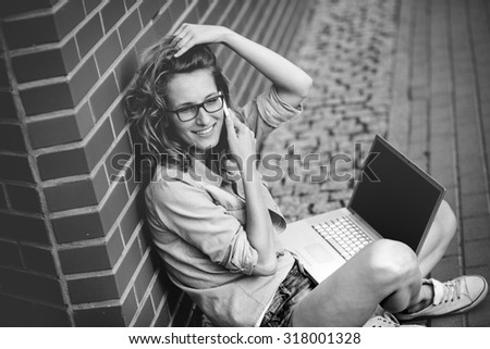 Beautiful student with laptop relaxing outside library. Portrait of female student outside library next to the brick wall