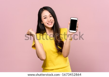 Portrait photo of young beautiful Asian woman feeling happy or surprise shock and holding smart phone with black empty screen on pink background can use for advertising or product presenting concept.