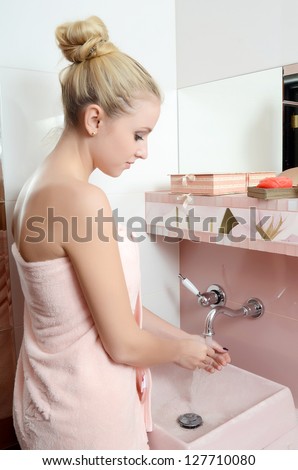 Woman blonde in pink towel washes hands