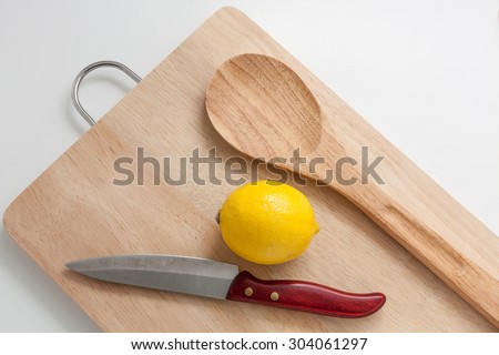Wooden cutting board with knife, wooden spoon and lemon on white background