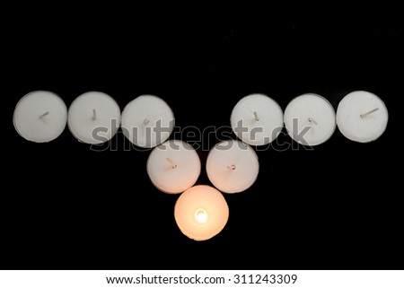 Tea lights candles arranged with one candle being lit on black background