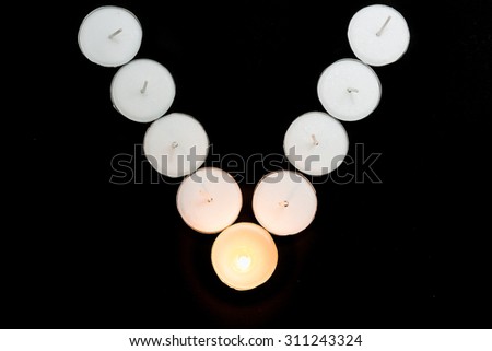 Tea lights candles arranged in v shape with one candle being lit on black background