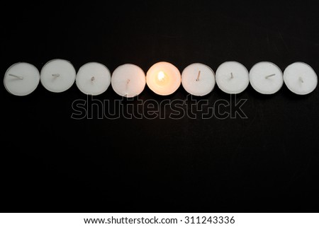 Tea lights candles arranged in line with one candle being lit on black background