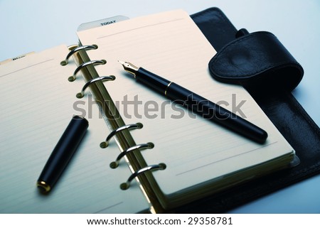Fountain pen with golden nib on open personal organizer. Cross-balanced.