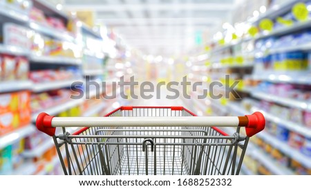 Supermarket aisle with empty red shopping cart.