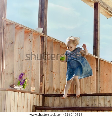 Little girl holding an apple and jumping on a country house wooden stairs, natural outdoor shot