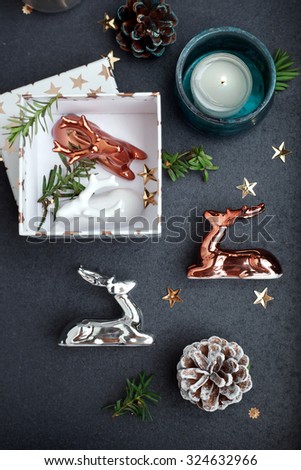 Modern style Christmas decor - ceramic reindeer in copper, silver and white colors, gift box and candles on coffee table. Natural light. Toned photo. Shallow focus.