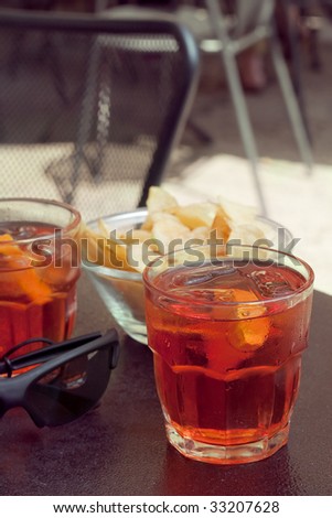 At the bar: two glasses with long drinks with oranges and potato chips on the table