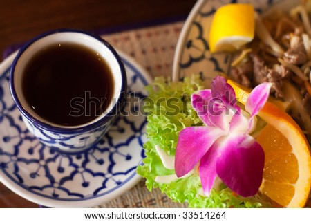 Lunch in a thai restaurant: thai noodles served beautifully with an orchid flower and a cup of tea, focus on the flower