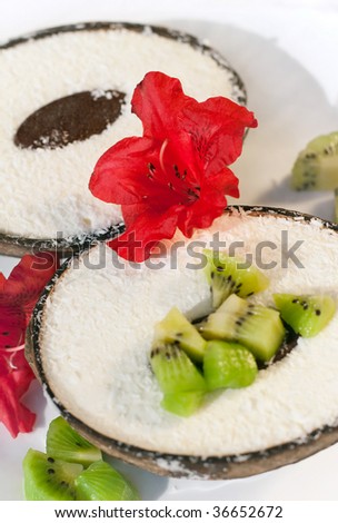 Closeup of ice-cream served in coconut halves with diced kiwi, decorated with red tropic flowers