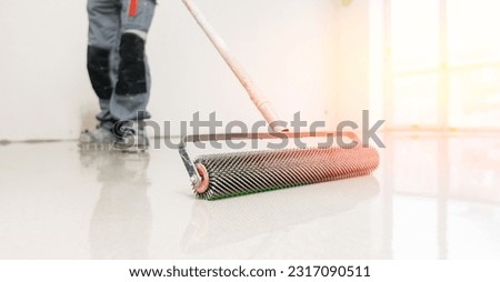 Master with needle roller for new screed concrete with mixture of cement for leveling for floors with sunlight, building renovation banner. Foto stock © 