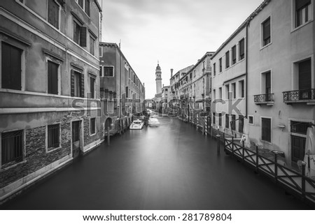 Long time exposure of canal in Venice (Venezia) with old buildings, boats and the leaning belfry tower of San Giorgio dei Greci, Italy, Europe, vintage black and white style