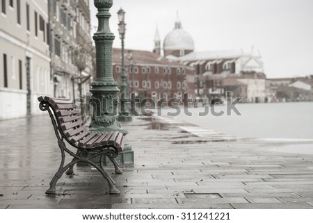 long time exposure of typical wooden bench on promenade in Venice (Venezia) on a rainy day in autumn without people, Italy, Europe