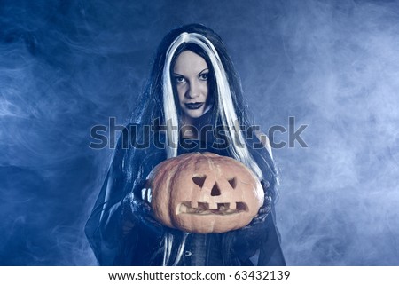 Portrait Halloween witch with a pumpkin. Smoke background
