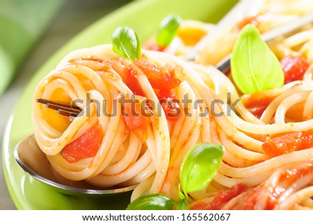 Spaghetti with tomato sauce swirled on a fork garnished with fresh basil leaves
