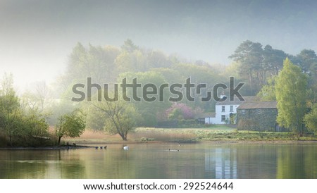 Stable Hill Farm at Derwent Water, Lake District, UK, on a misty spring morning, with ducks, swans and reflections of the house and trees in the water.