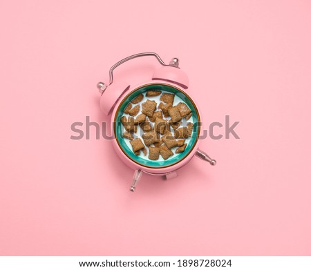 Top view flat lay creative collage with  pink alarm clock and breakfast crunchy pillows with milk a pastel pink background. Breakfast and good morning concept. 