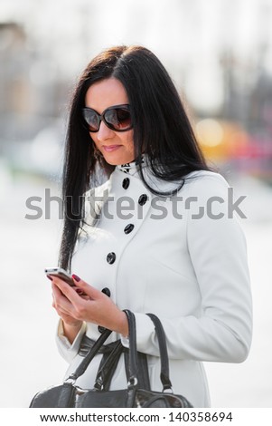 Beautiful brunette woman looking at mobile phone outdoor (shallow dof)