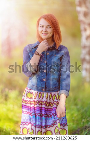 Young ginger-haired woman walking on nature beneath sunbeams in summer day (shallow dof)