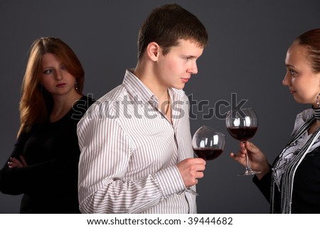 Young couple holding glasses with wine and woman looking at them, studio, gray background