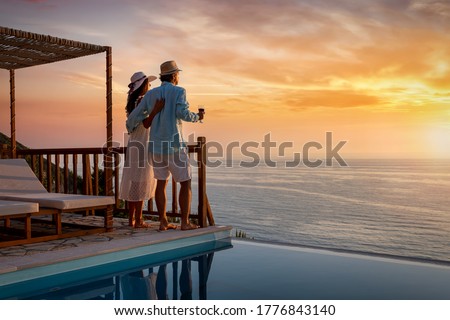 A romantic couple on summer vacation enjos the sunset over the mediterranean sea by the pool with a glass of Aperitif