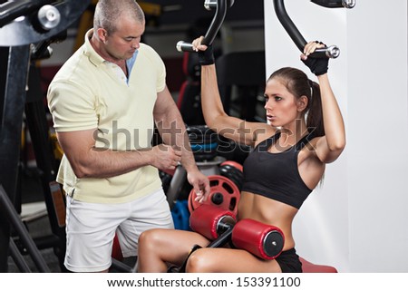 Woman at the health club with her personal trainer, learning the correct form on the pulldown machine.