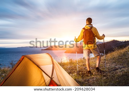 Backpacker looking at beautiful sunrise at big lake near tent